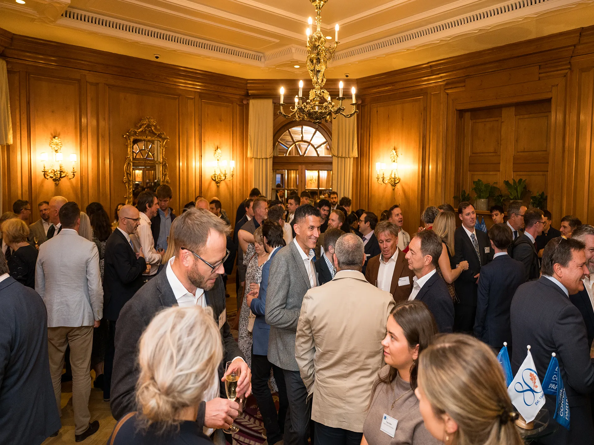 People standing and chatting holding champagne glasses in a wood panelled room